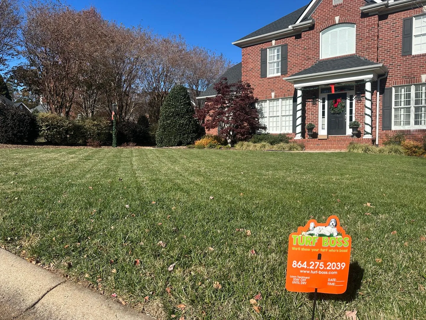 A neatly mowed lawn in front of a brick house, with a Turf Boss yard sign near the curb.
