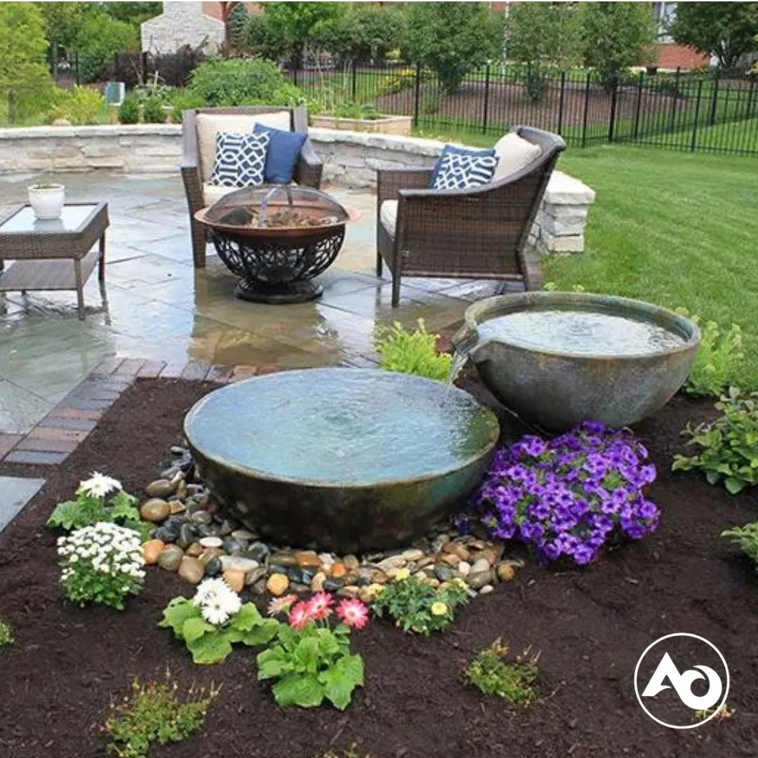 Two round water features surrounded by flowers, with patio seating in the background.